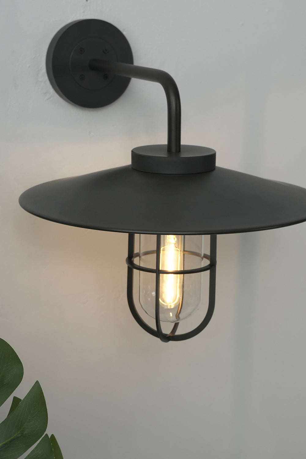Lit black Portree wall light in studio setting | Metal, Glass | Close-up showing warm bulb glow | Samu Lamp