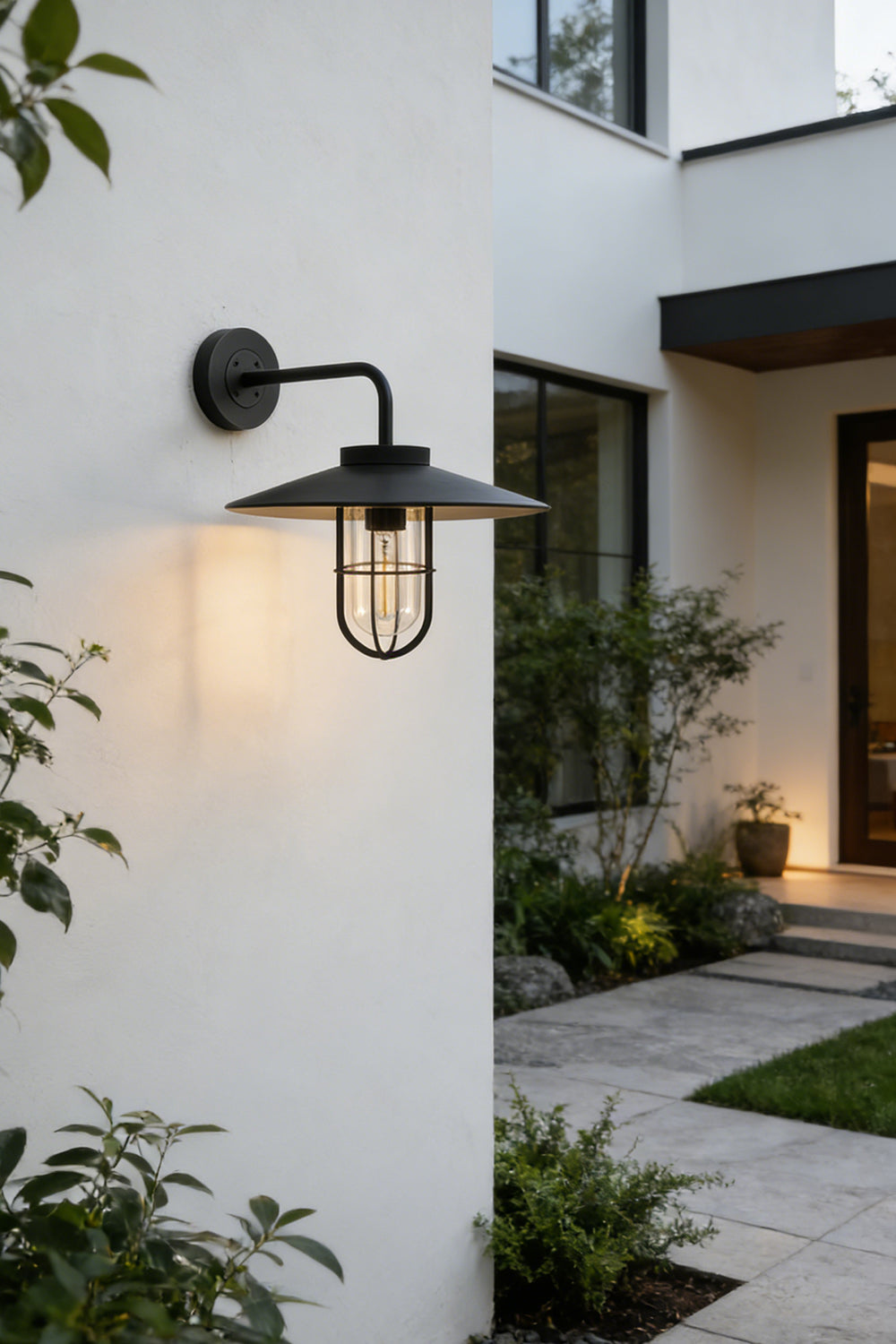Black Portree wall light lit at night on a house wall | Metal, Glass | Evening exterior shot with garden landscaping | Samu Lamp