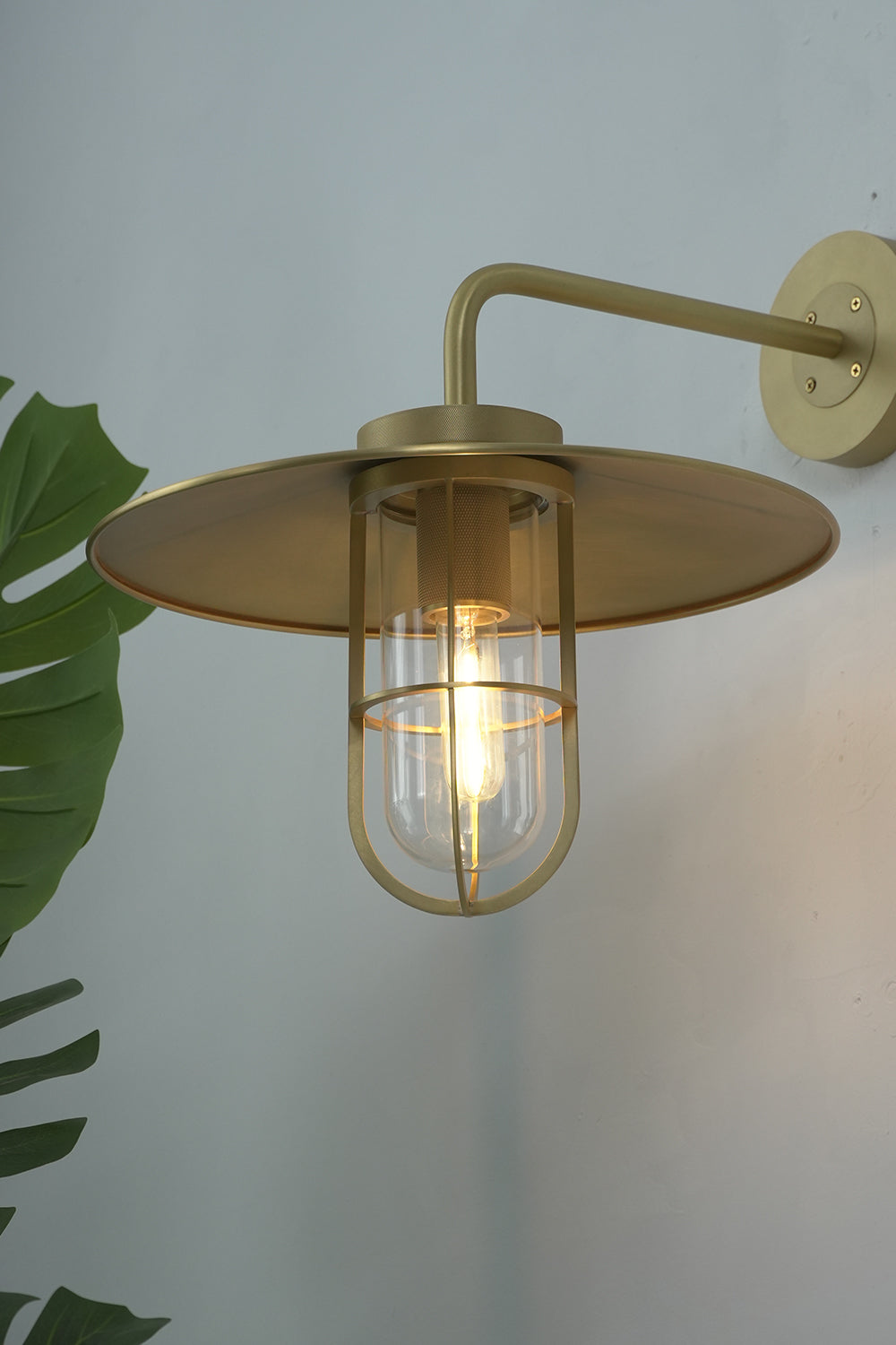 Close-up of lit brass Portree wall sconce | Brass, Glass | Showing the glass cylinder and protective cage | Samu Lamp