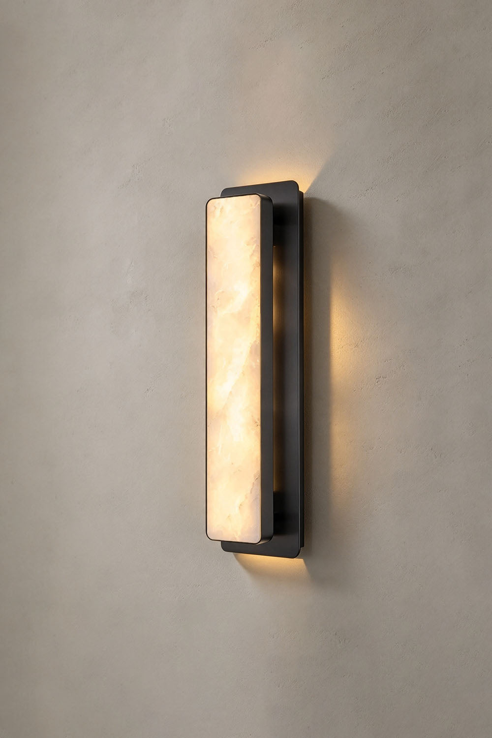 Quadrelle Wall Sconce | Alabaster and Bronze | Front view of bronze variant illuminated on grey plaster wall | Samu Lamp