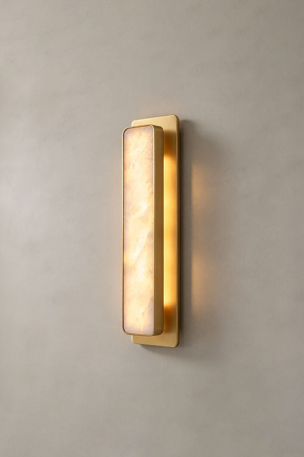 Quadrelle Wall Sconce | Alabaster and Brass | Front view of brass variant illuminated on grey plaster wall | Samu Lamp