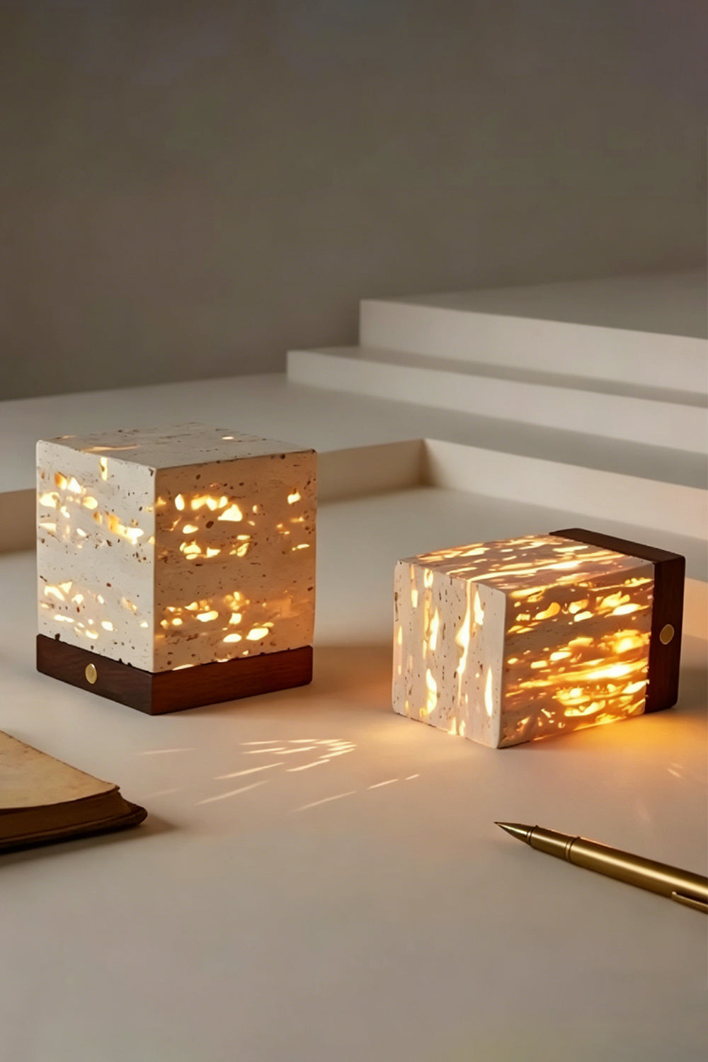 Radiant Monolith Travertine Table Lamp | Travertine, Wood | Pair of lamps on stepped platform | Lit and unlit variations shown | Intricate internal light patterns | Samu Lamp