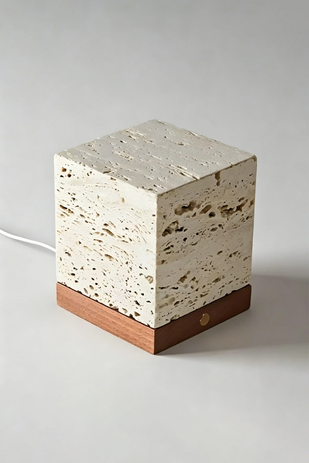 Radiant Monolith Travertine Table Lamp | Travertine, Wood | Unlit angled view on grey surface | Porous stone voids detail | Dark wood base | Samu Lamp
