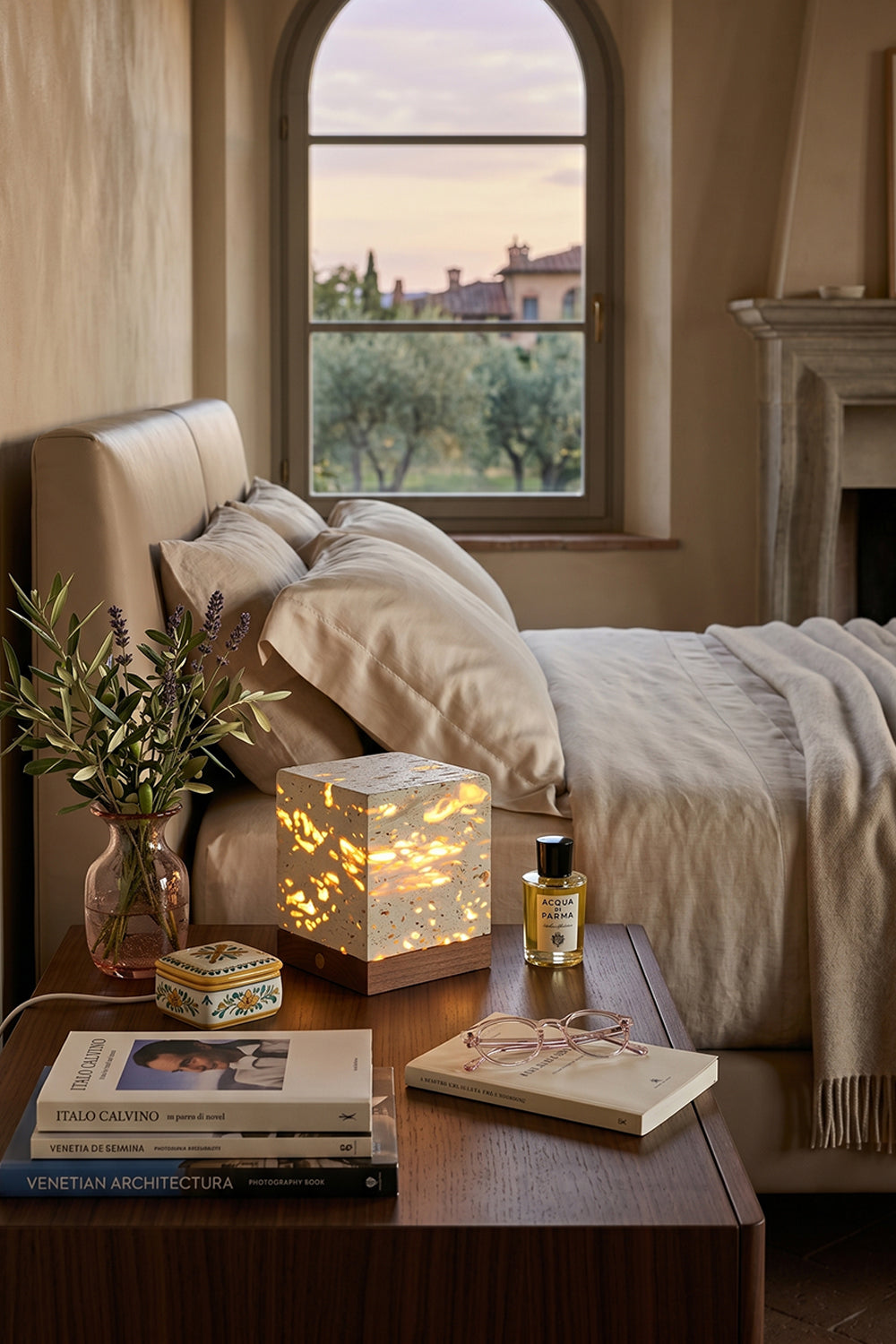 Radiant Monolith Travertine Table Lamp | Travertine, Wood | Lit on wood nightstand | Tuscan bedroom landscape view | Arched window frame, hills | Samu Lamp