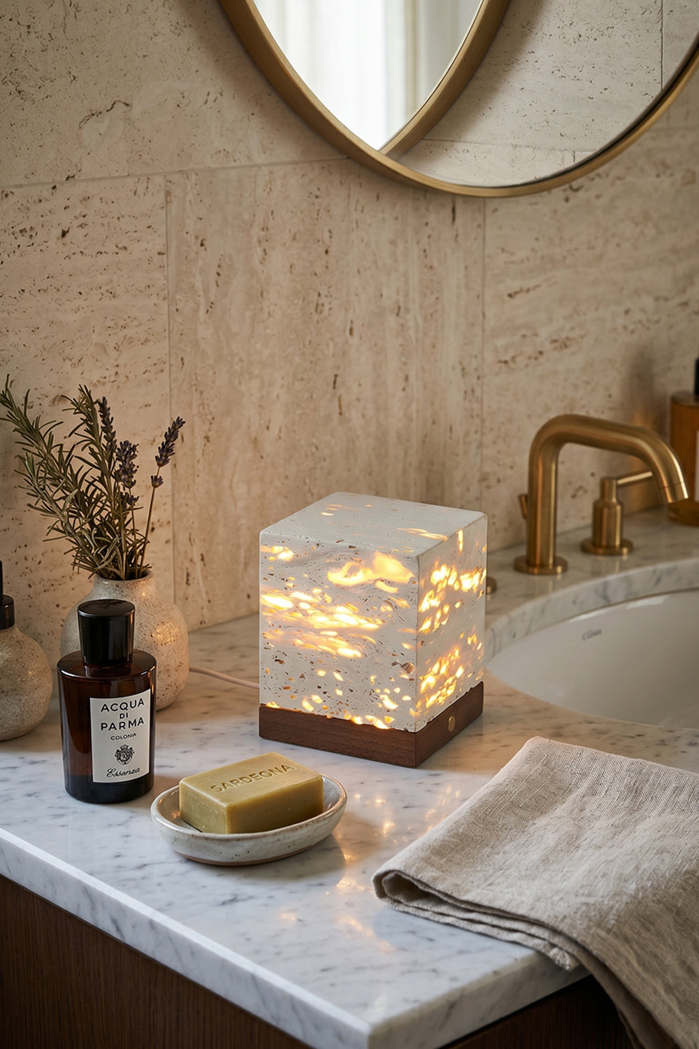 Radiant Monolith Travertine Table Lamp | Travertine, Wood | Unlit on marble vanity | Spa-like bathroom corner | Round mirror, toiletries, towels | Samu Lamp
