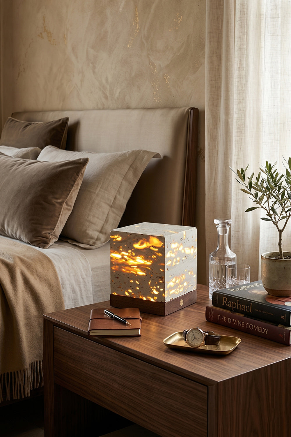 Radiant Monolith Travertine Table Lamp | Travertine, Wood | Lit on dark wood nightstand | Rustic bedroom setting | Textured wall, linen bedding | Samu Lamp
