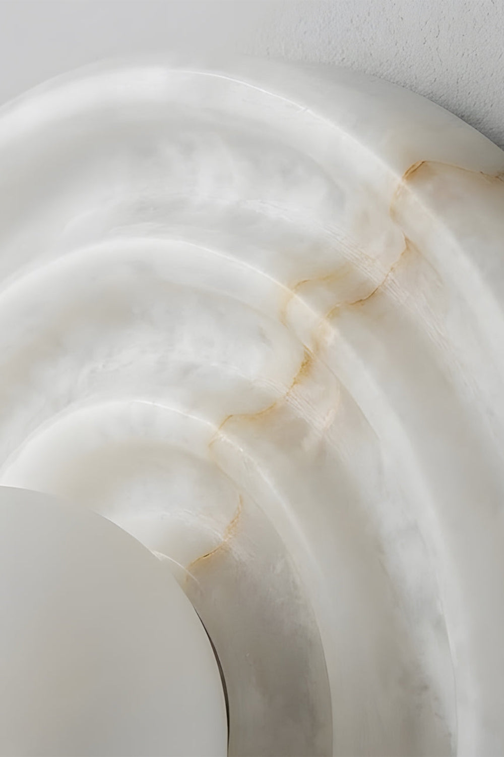 Rhea Rippled Alabaster Wall Sconce | Alabaster Ripple Detail | Close-up focus highlighting the intricate concentric carved ripples and subtle golden-brown mineral veins of the natural white stone | Detail shot | Samu Lamp