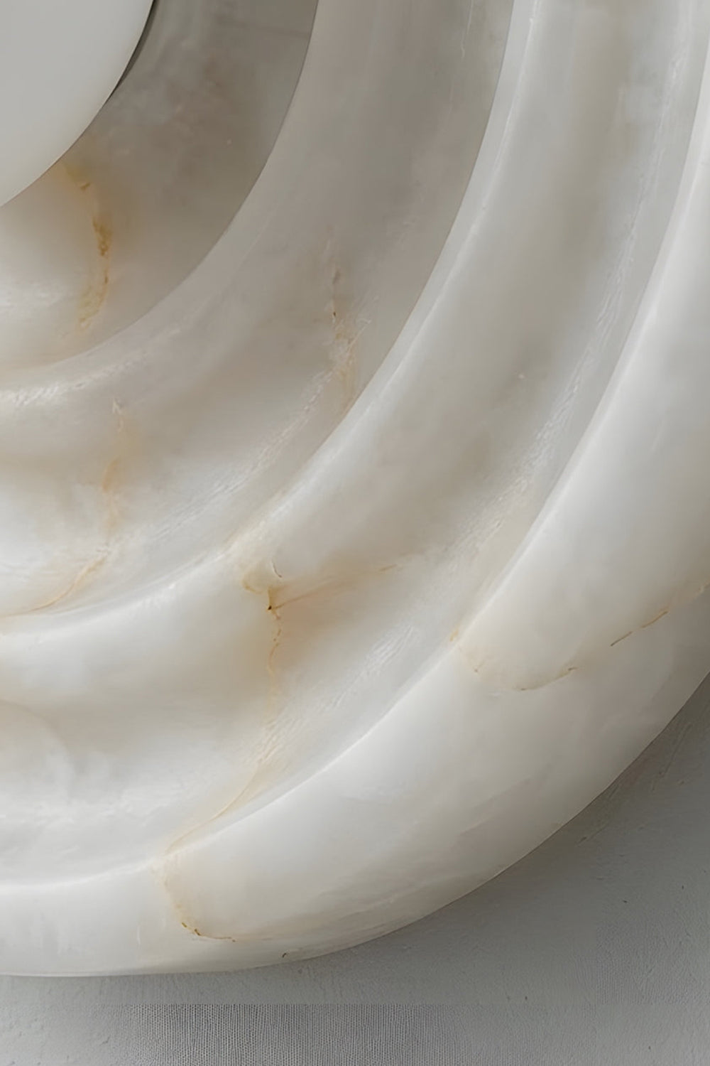 Rhea Rippled Alabaster Wall Sconce | Concentric Grooves Detail | Macro close-up view showing the sculptural layered depth of the circular rippled alabaster plate under soft lighting | Detail shot | Samu Lamp