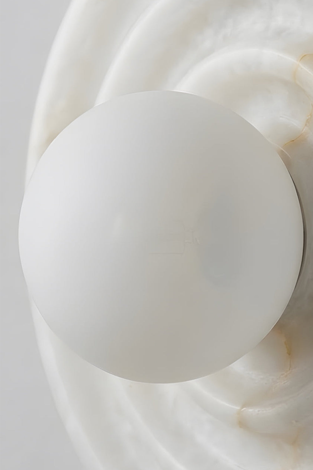 Rhea Rippled Alabaster Wall Sconce | Frosted Globe Detail | Detailed close-up shot focusing on the central frosted white glass sphere orb bulb sitting neatly within the carved stone ripples | Detail shot | Samu Lamp