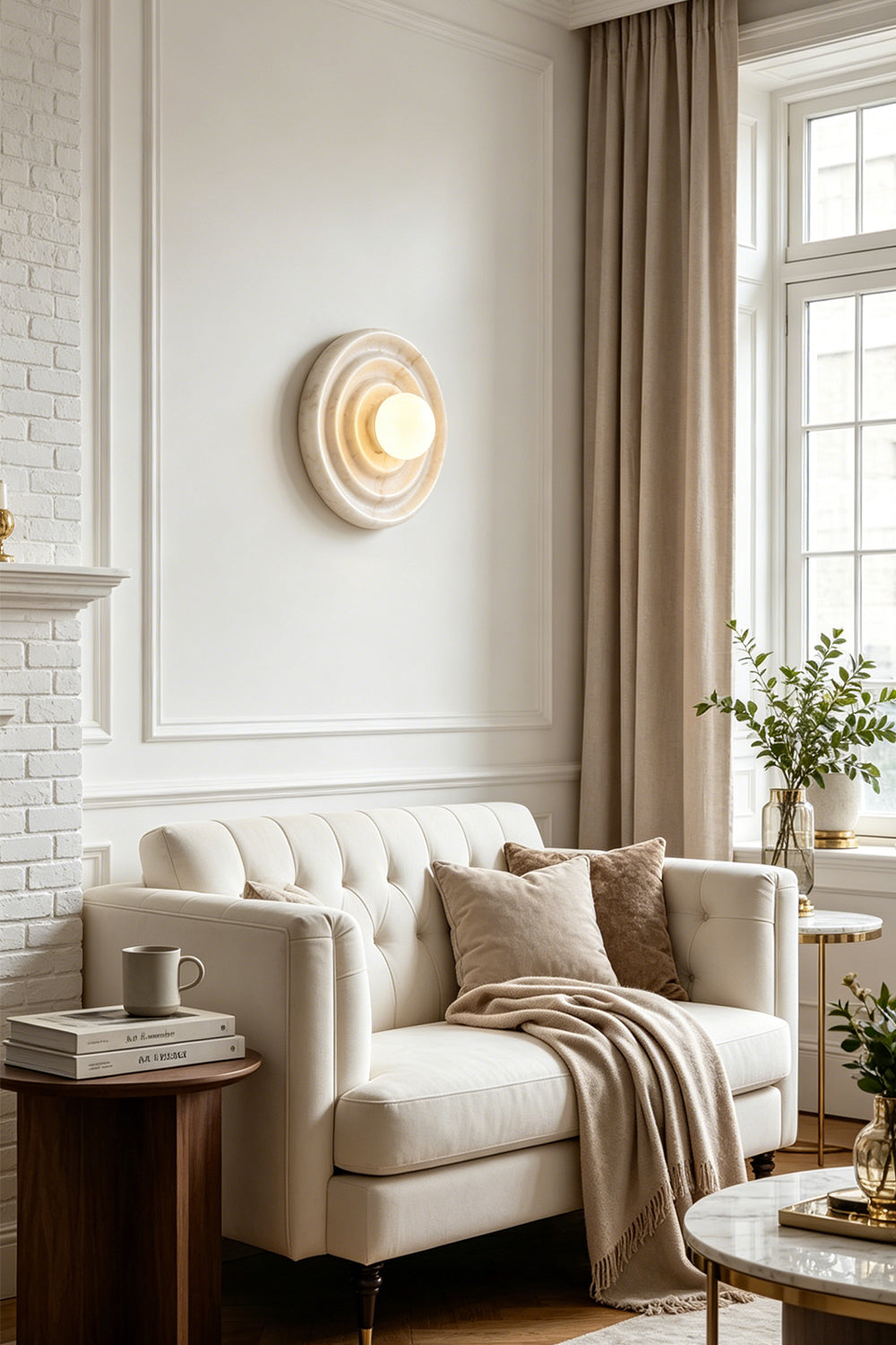 Rhea Rippled Alabaster Wall Sconce | Living Room Ambient Light | Providing a warm ambient glow on a white paneled wall above a classic cream sofa paired with taupe window drapes | Samu Lamp