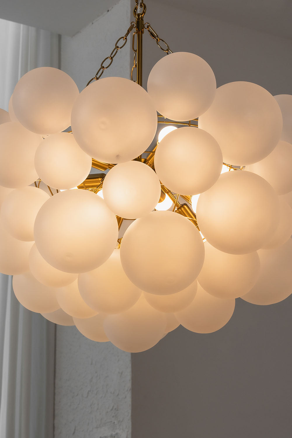 Romilly Frosted Globe Cluster Chandelier | Frosted Glass and Brass | Medium close-up of the glowing frosted glass globe cluster against a grey background | Samu Lamp