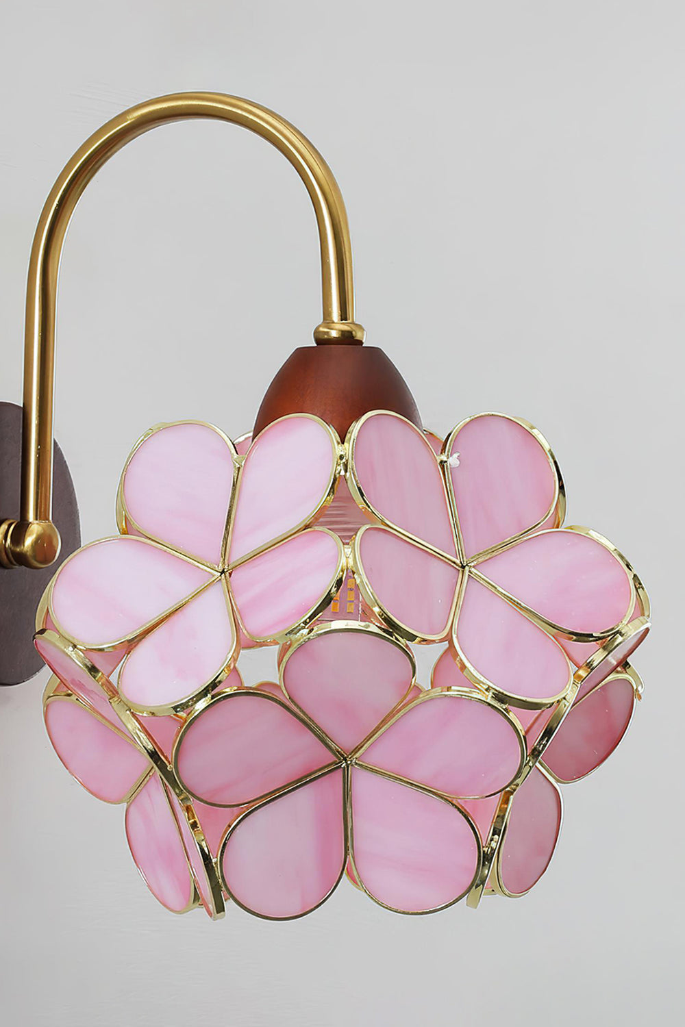 Rosalind Petal Glass Botanical Wall Lamp | Glass, Metal, Wood | Side angled view of the lit pink flower petal wall light casting a soft pinkish-gold halo on a plain studio wall | Samu Lamp
