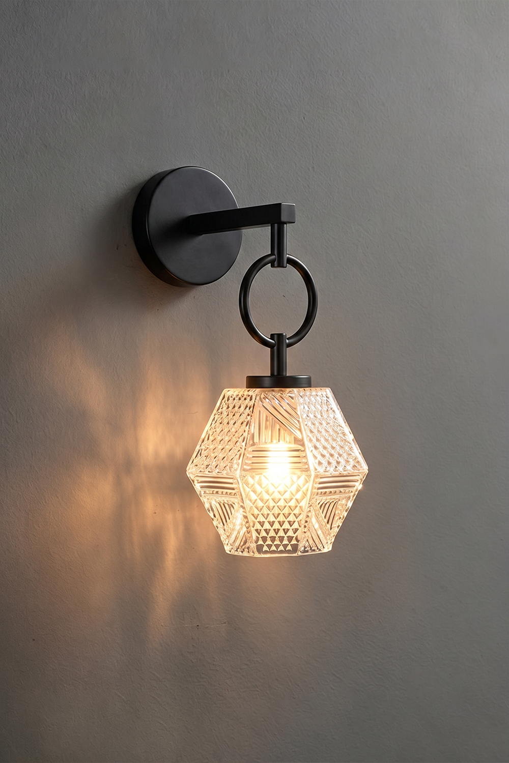Rosamund Faceted Glass Wall Sconce | Faceted Glass and Black Metal | Matte black finish version illuminated against a dark grey wall | Samu Lamp
