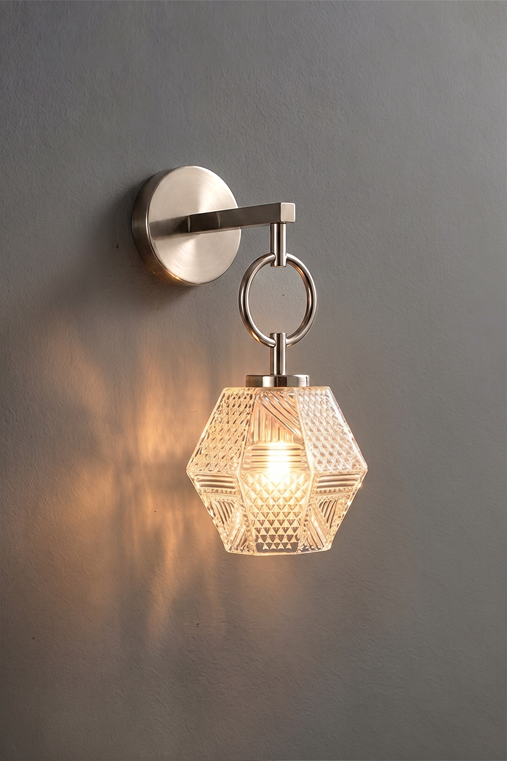 Rosamund Faceted Glass Wall Sconce | Faceted Glass and Silver Metal | Brushed nickel finish version glowing against a dark background | Samu Lamp