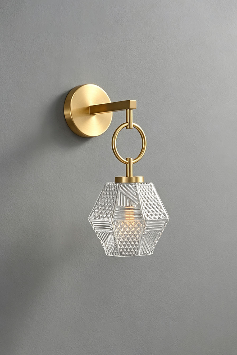 Rosamund Faceted Glass Wall Sconce | Faceted Glass and Brass | Unlit front view of the brass sconce on a grey wall | Samu Lamp