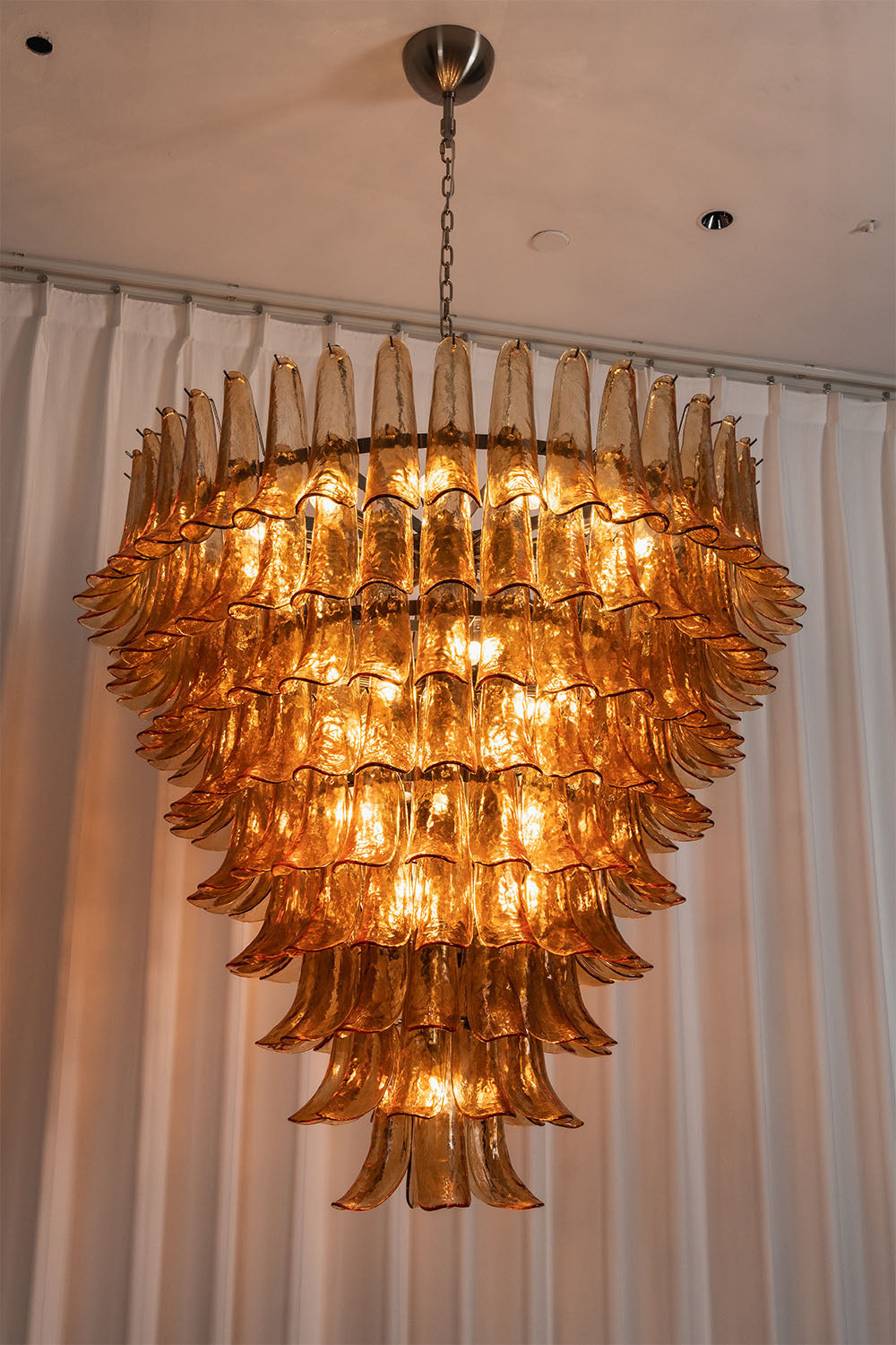 Rouveline Rippled Amber Glass Cone Chandelier | Rippled Amber Glass and Metal | Real-life view illuminated gracefully against white window drapes | Samu Lamp
