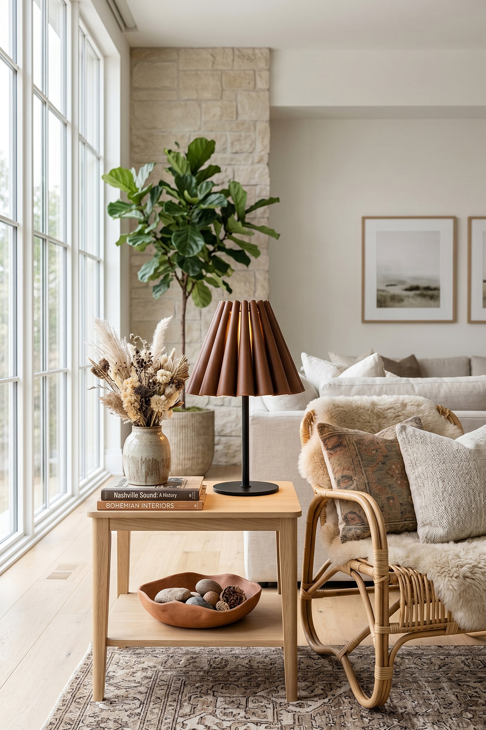 Rowan Leather Pleated Table Lamp | Leather, Metal | Placed on a light oak side table next to a woven armchair and a large window in a bright living room | Samu Lamp
