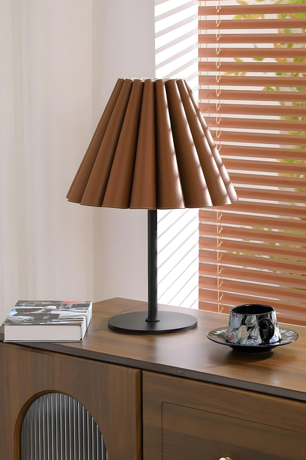 Rowan Leather Pleated Table Lamp | Leather, Metal | Situated on a sleek dark wood sideboard cabinet near window blinds in a contemporary workspace | Samu Lamp