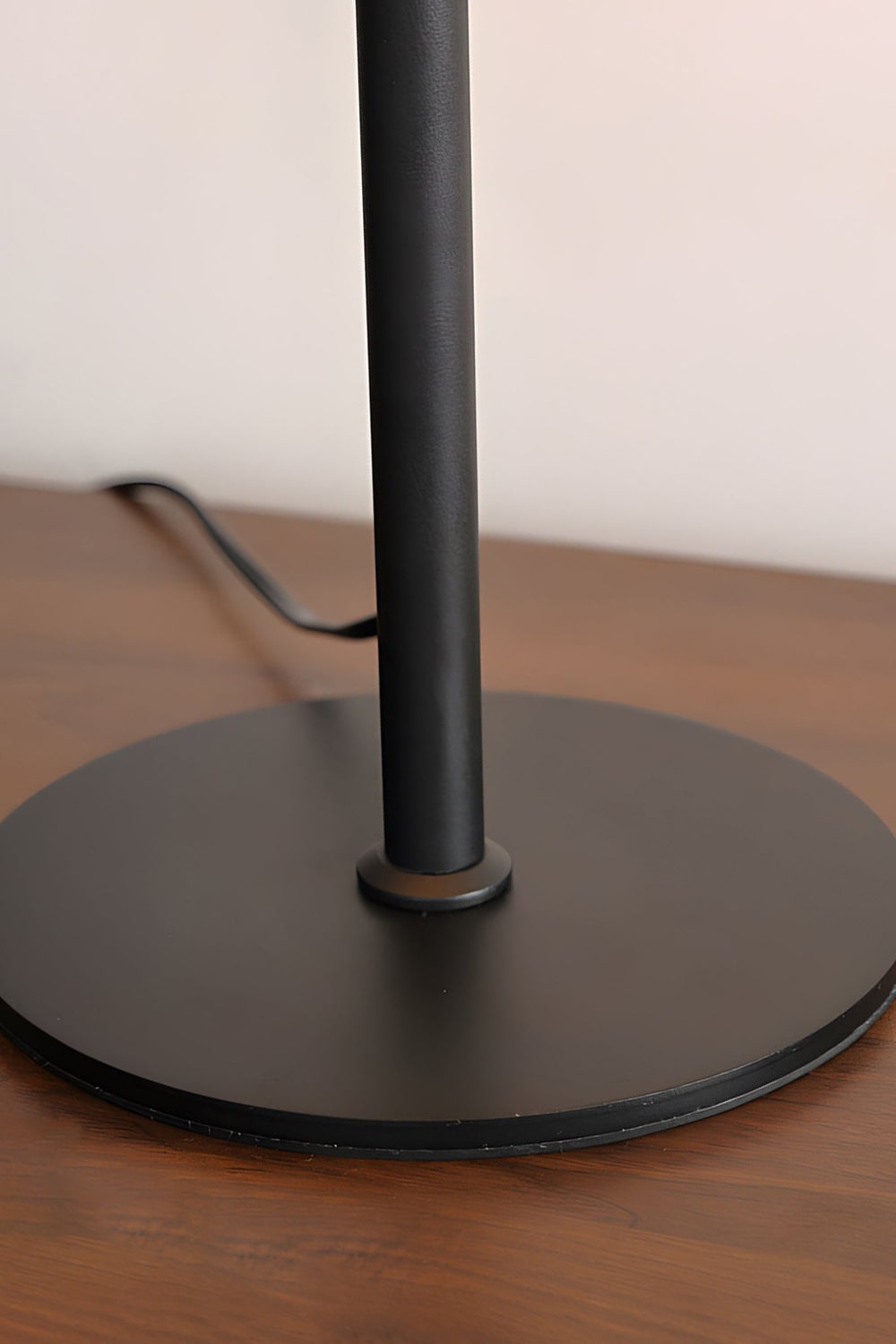 Rowan Leather Pleated Table Lamp | Leather, Metal | Close-up focus on the flat circular matte black metal base plate resting on a polished wooden surface | Detail shot | Samu Lamp