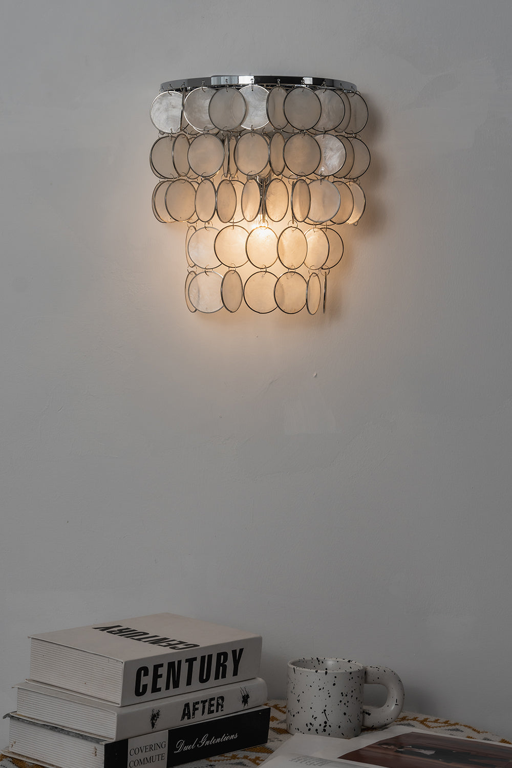 Lit Shimmering Round Capiz Wall Lamp | Shell | Iron | Mood shot above books in a dark corner | Samu Lamp