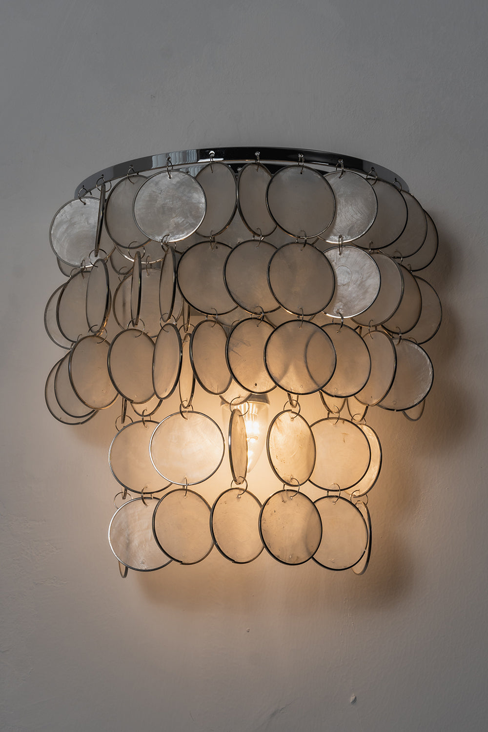 Front view of lit Capiz wall sconce | Shell | Iron | Product shot against a neutral studio background | Samu Lamp