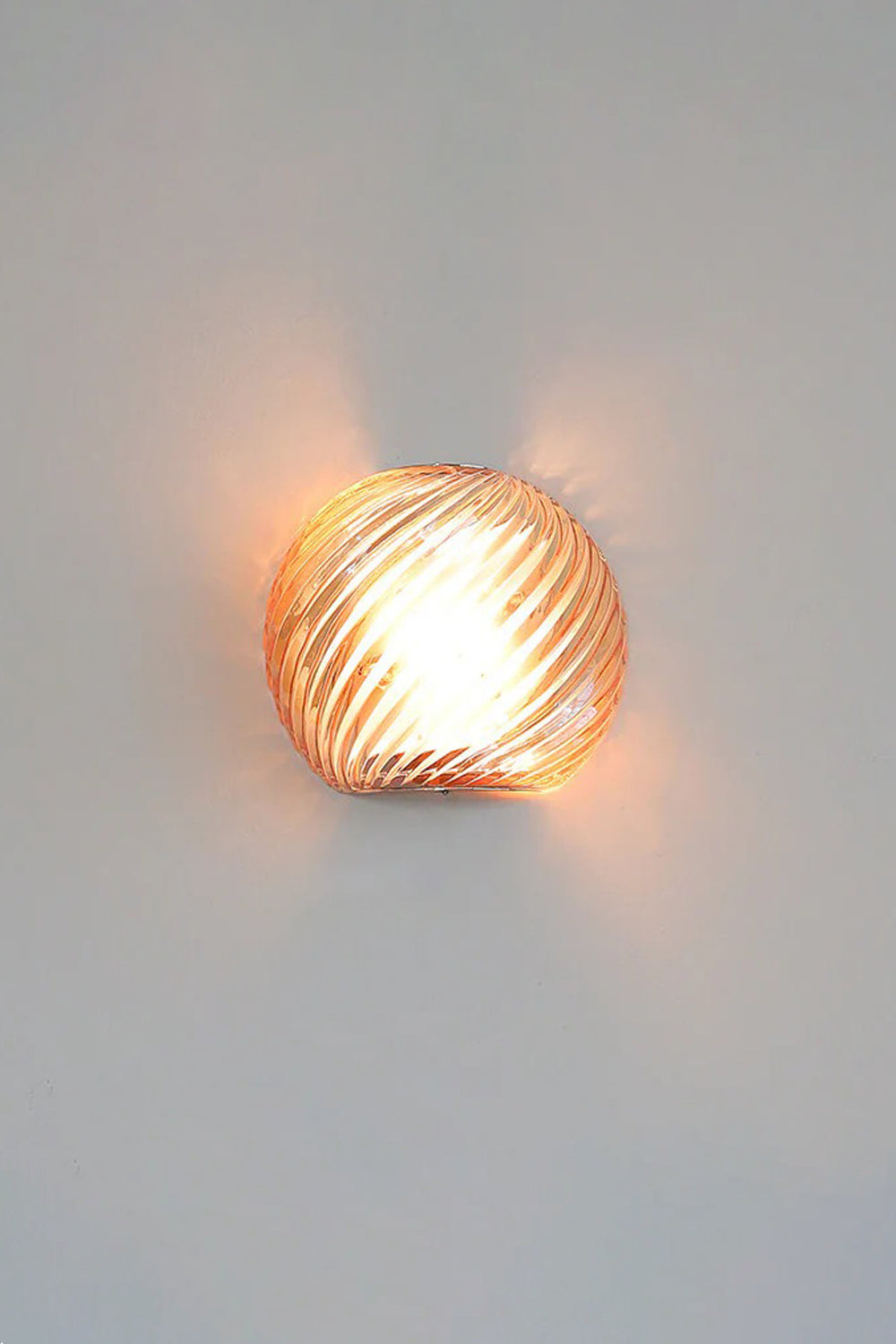 Silas Ribbed Glass Wall Sconce | Ribbed Glass, Metal | Staged illuminated view of the amber glass finish option radiating a rich orange-gold light halo on a light grey wall | Samu Lamp