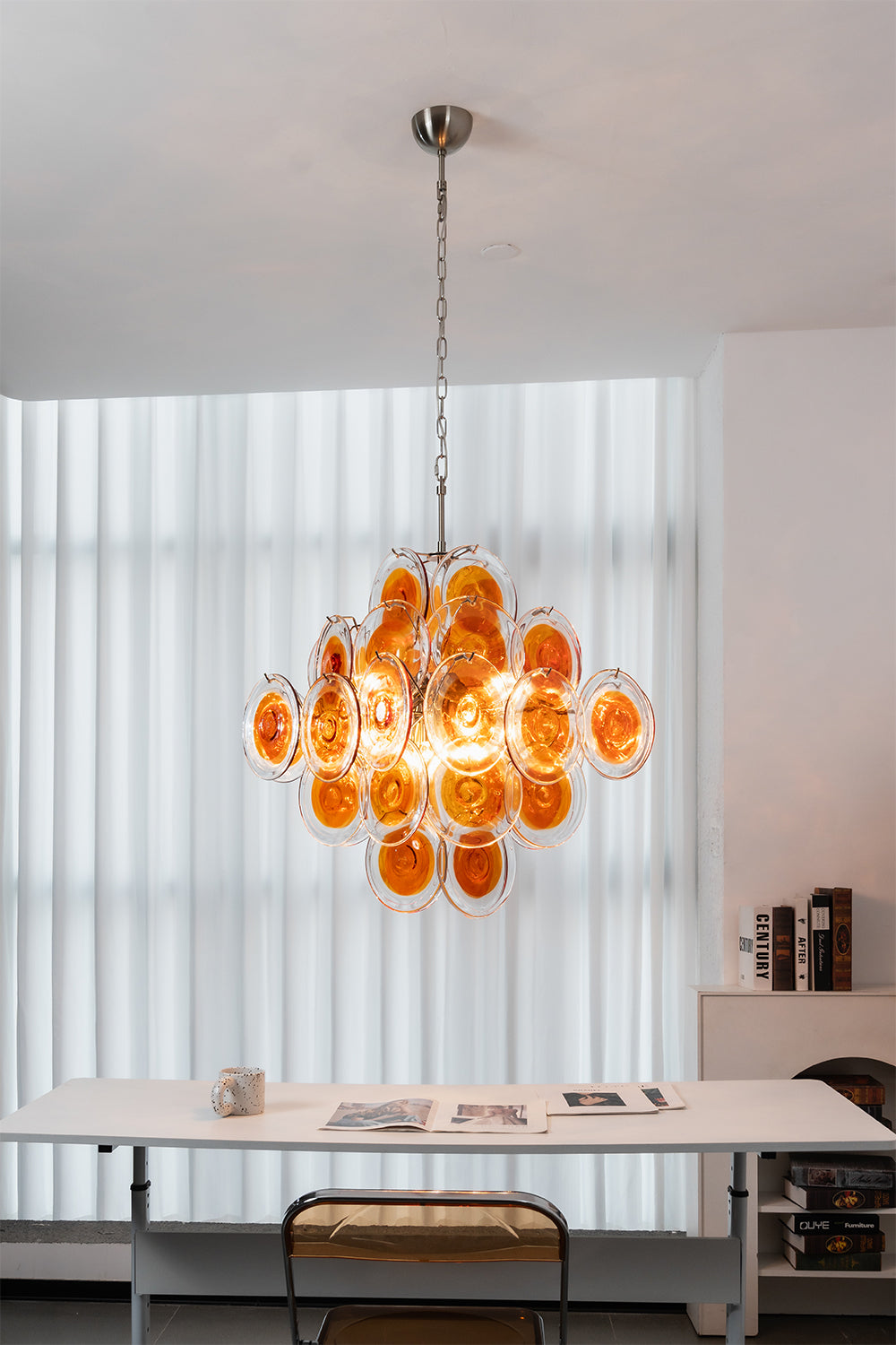 Modern tiered chandelier with amber glass discs | Metal, Glass | Installed in a minimalist work area with white furniture | Samu Lamp