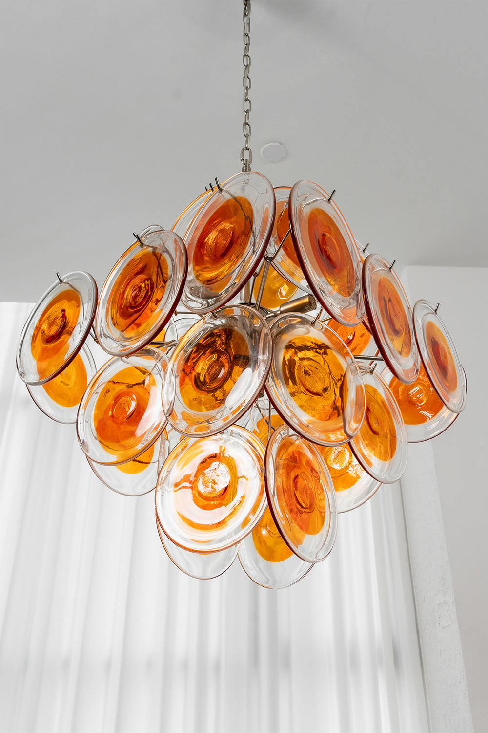 Angled view of Solari Amber Glass Chandelier | Metal, Glass | Hanging against white curtains and bright window | Samu Lamp