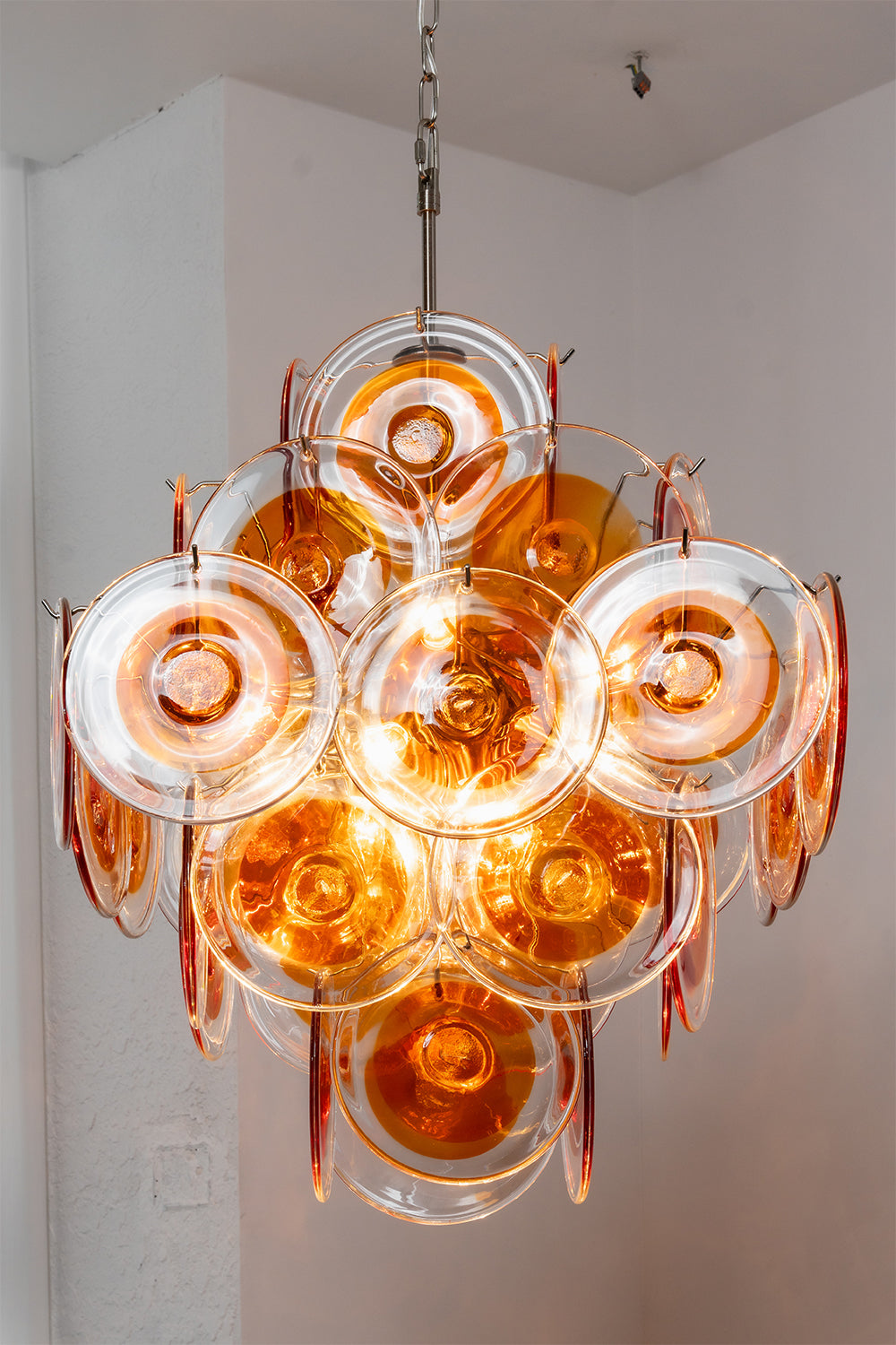 Lit amber glass chandelier showing warm glow | Metal, Glass | Warm ambient lighting effect in a clean space | Samu Lamp