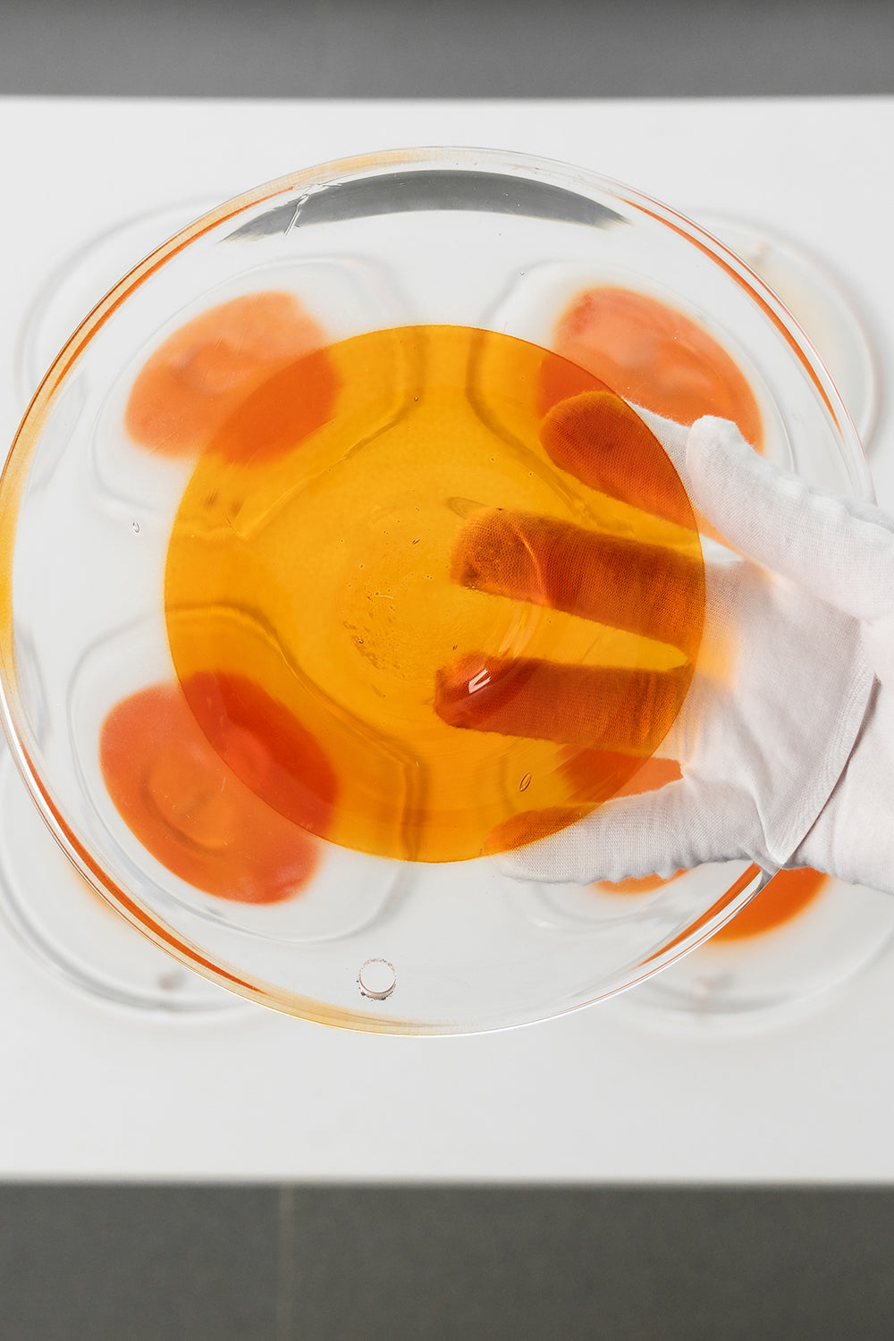 Close-up of a circular amber glass disc | Glass | Detail shot of a single disc being handled with a glove | Samu Lamp