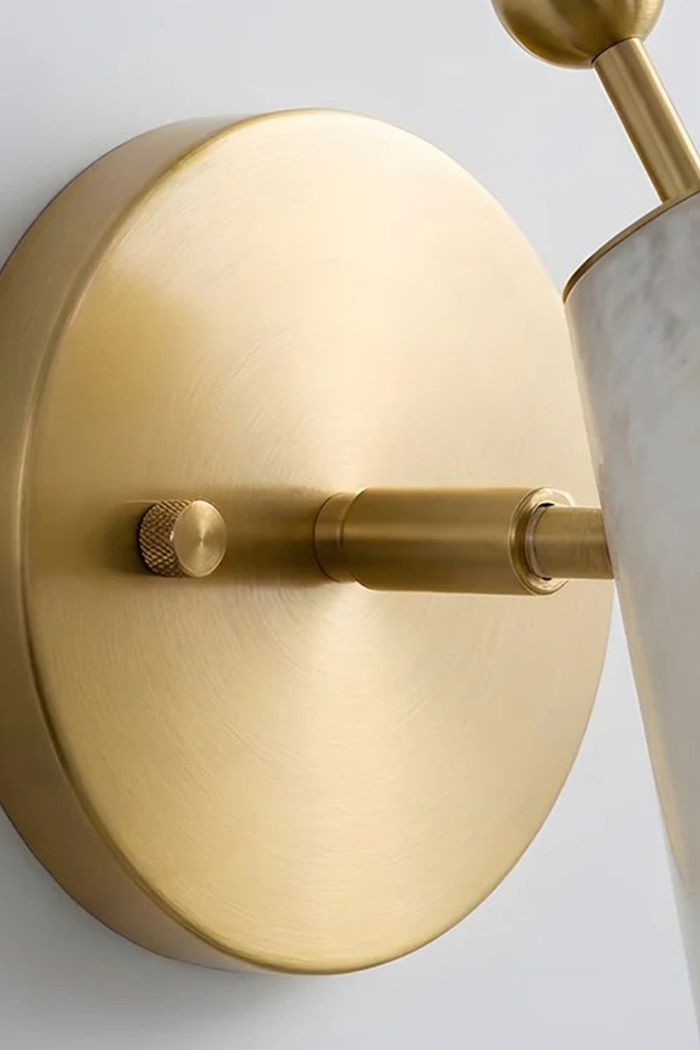 Solene Alabaster Cone Wall Sconce | Alabaster, Brass | Close-up detail view of the circular brushed brass wall mounting plate and connection arm hardware showcasing premium metallic finish | Detail shot | Samu Lamp