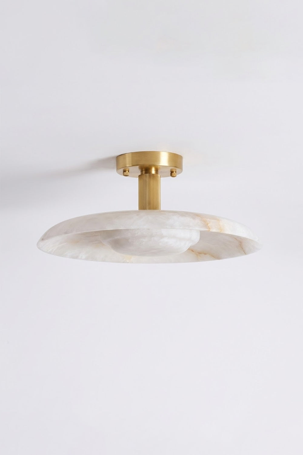 Solene Alabaster Round Ceiling Light | Studio Hanging Shot | Angled studio view of the fully lit round stone flush mount fixture casting a warm golden glow against a light backdrop | Samu Lamp