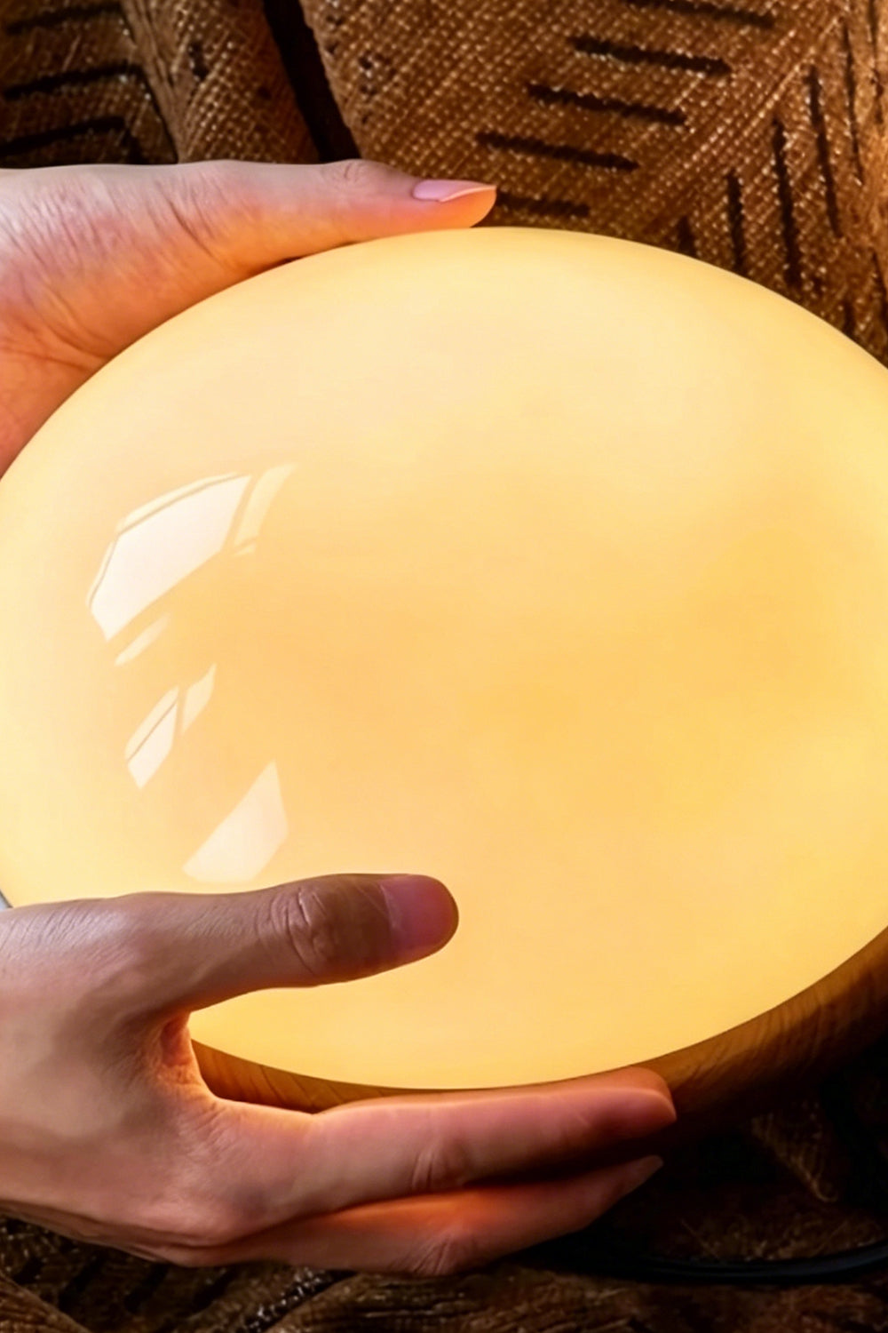 Soren Wood Grain Pendant Lamp | Wood, Glass, Metal | Close-up reference view of hands holding the fully illuminated glowing glossy glass diffuser bowl | Detail shot | Samu Lamp