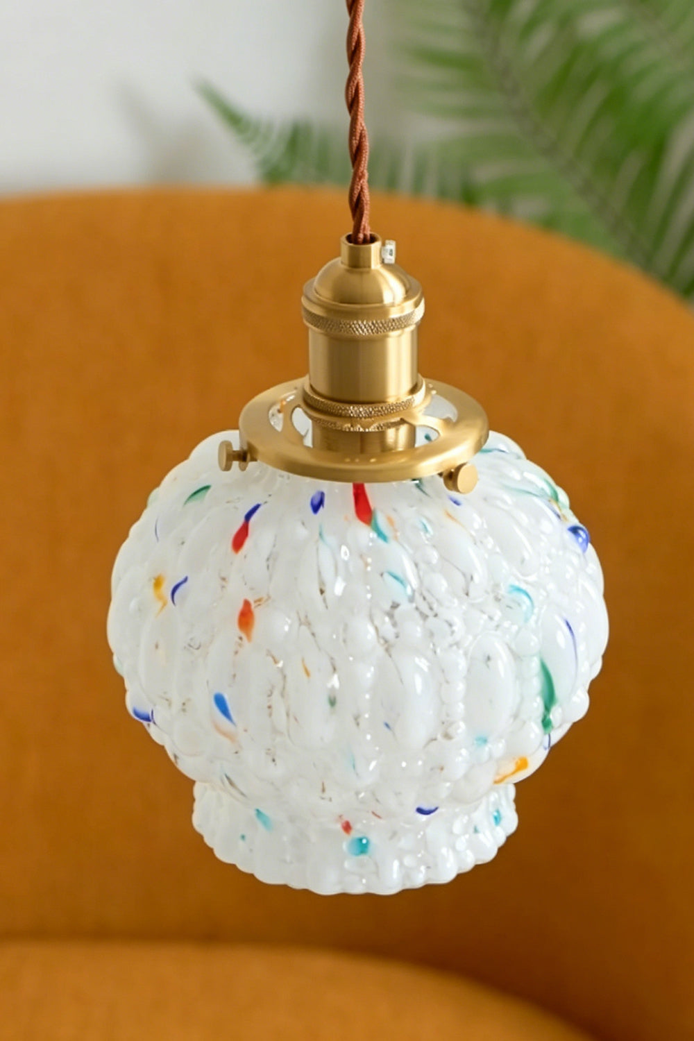 Speckled Bubble Glass Pendant Lamp | Glass, Metal | Frontal view of the unlit white speckled glass pendant hanging elegantly against a warm mustard orange chair backdrop | Samu Lamp