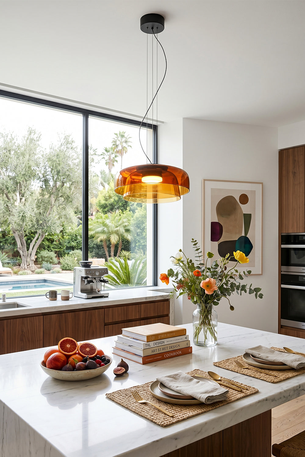 Stratum Layered Glass Pendant Light | Glass, Metal | Orange variant hanging as a warm centerpiece over a modern white kitchen island with flowers | Samu Lamp
