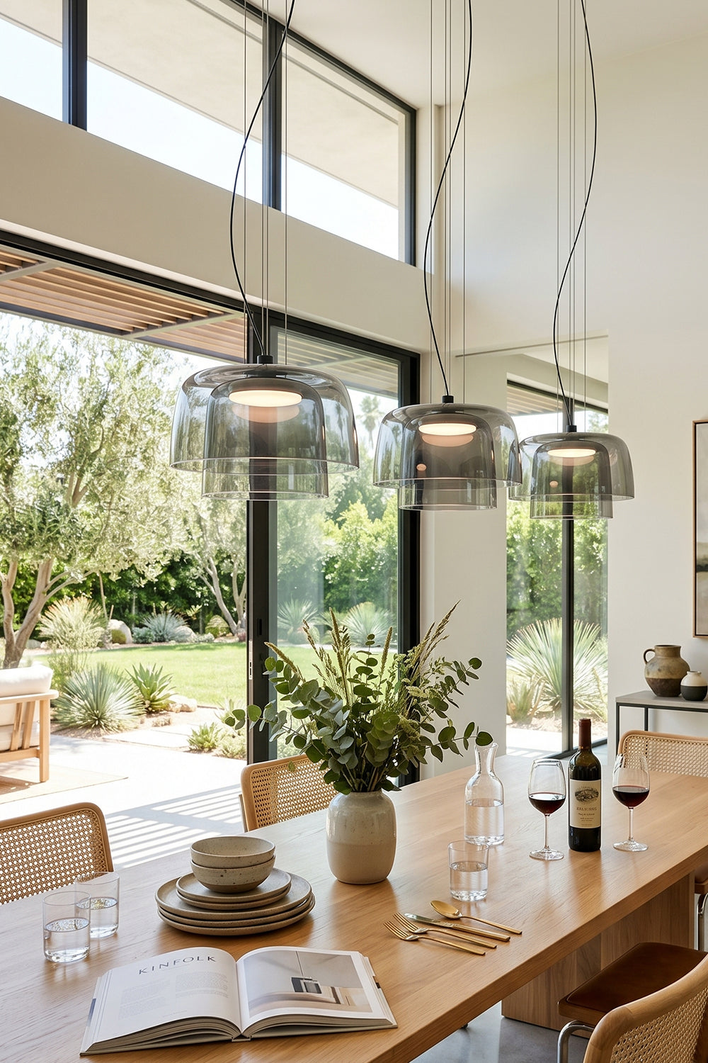 Stratum Layered Glass Pendant Light | Glass, Metal | A trio of smoky grey pendant lights lined up over a long wooden dining table facing a sunlit garden | Samu Lamp