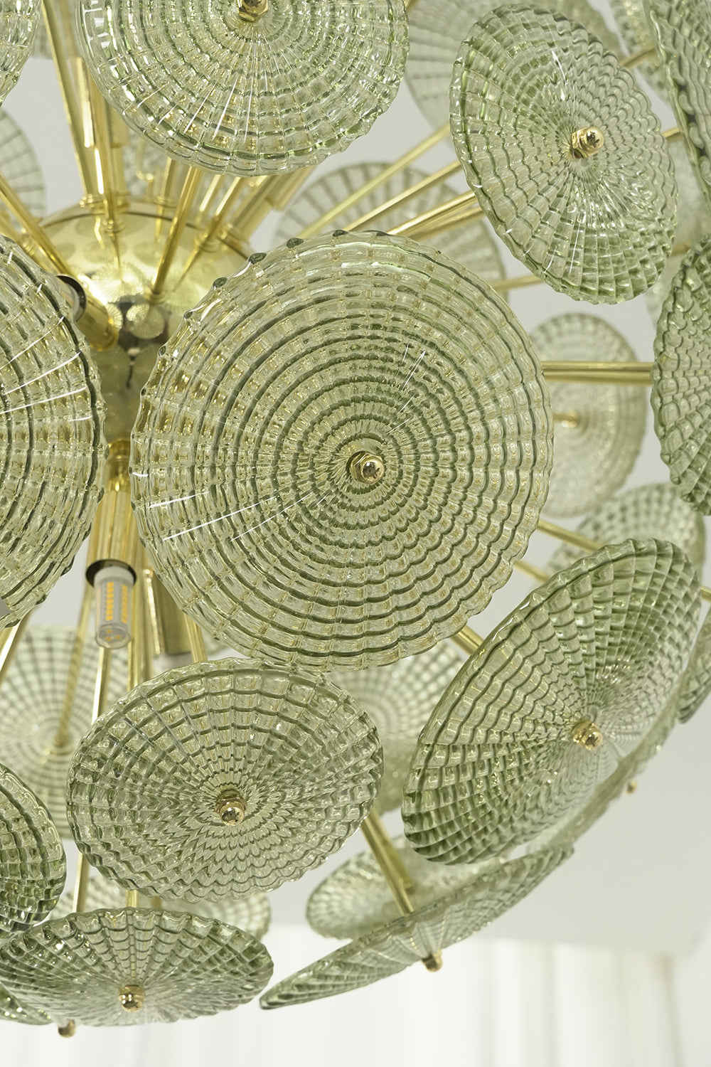 Detailed close-up of unlit green glass sunburst discs | Metal, Glass | Showing texture and brass attachment hooks | Samu Lighting