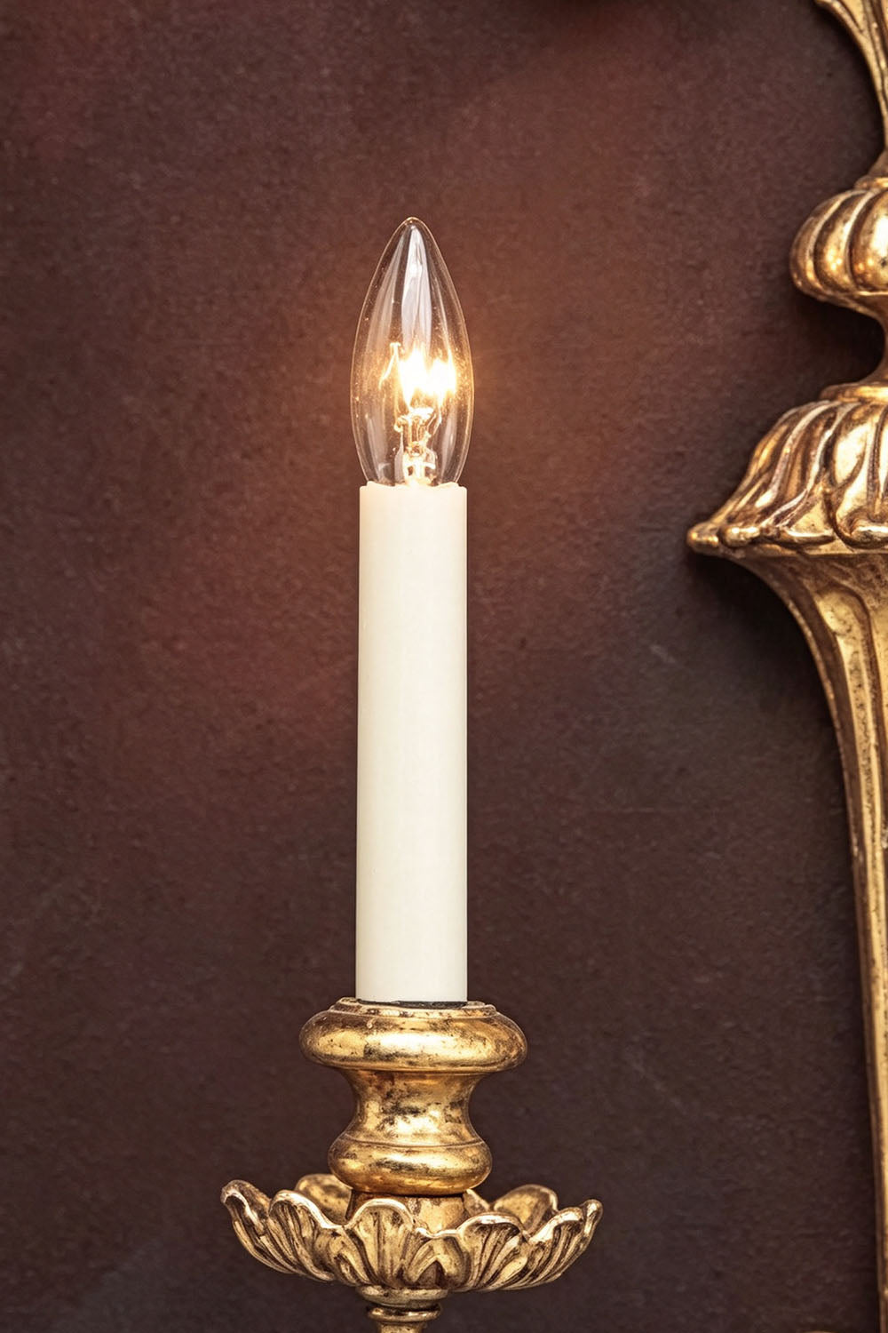 Tamsin Carved Plume Candle Wall Lamp | Carved Resin and Brass | Close-up view of a single candle light glowing against a dark textured background | Samu Lamp