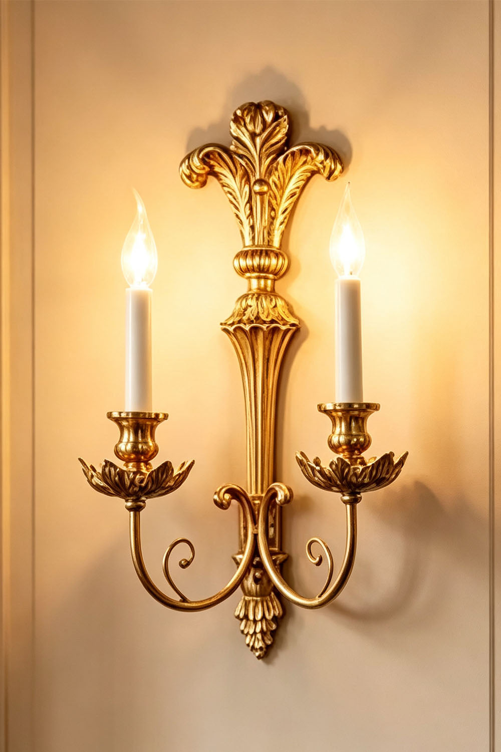 Tamsin Carved Plume Candle Wall Lamp | Carved Resin and Brass | Full view of the double candle sconce glowing warmly on a plain wall | Samu Lamp