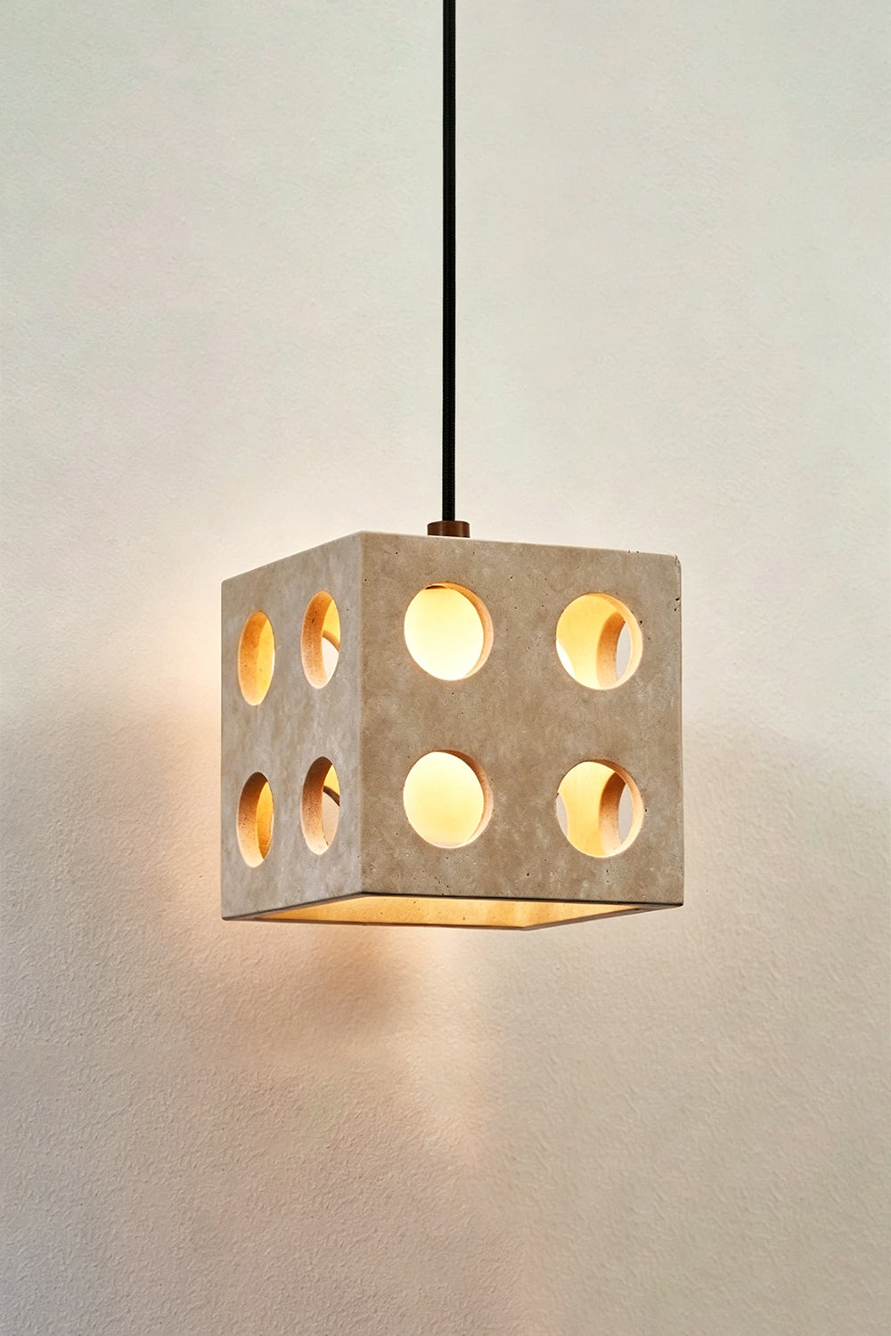 Terra Cube Travertine Pendant Light | Travertine, Metal | Lit product detail shot against textured wall | Samu Lamp