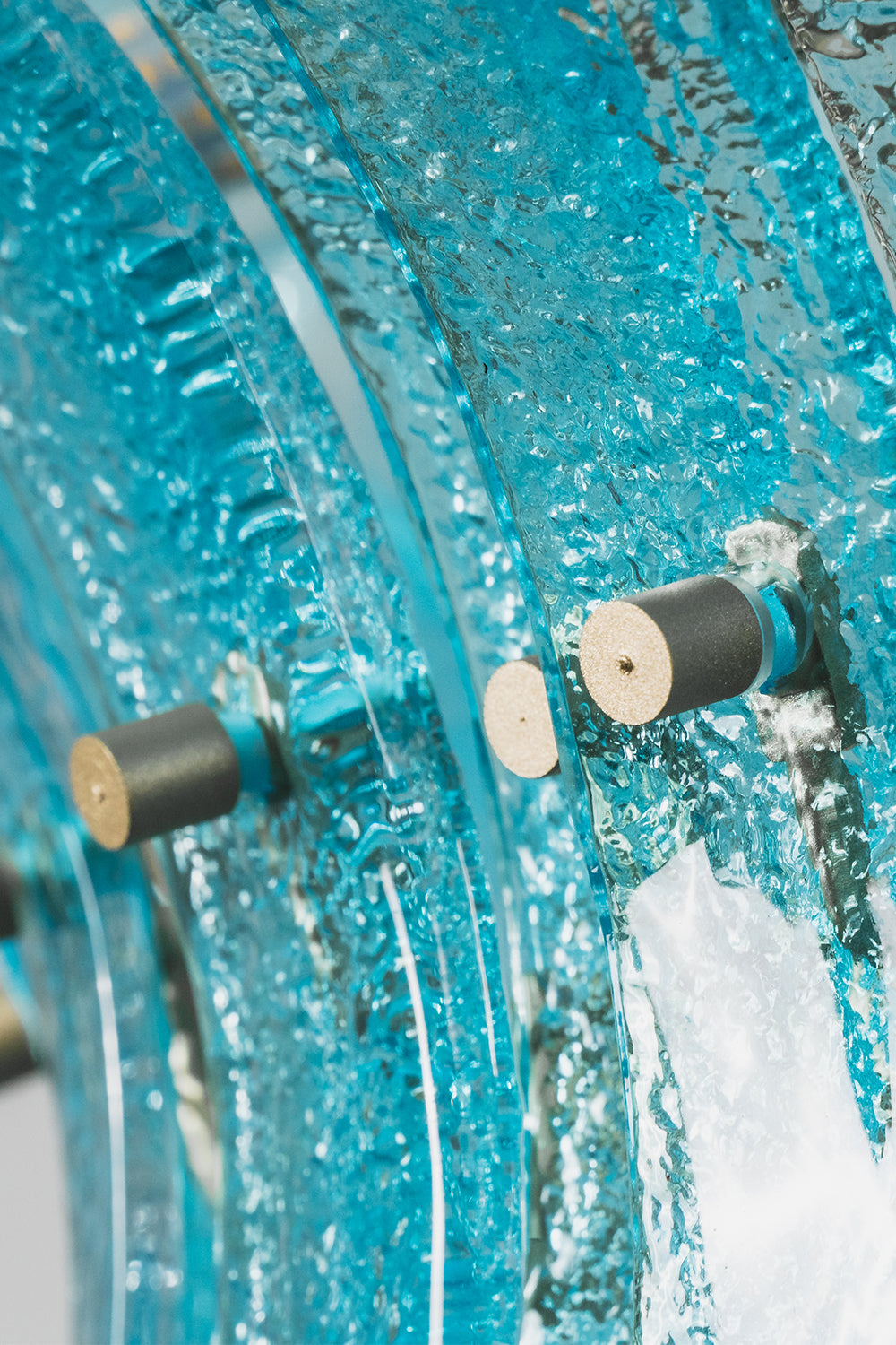 Thalassa Aquamarine Textured Glass Chandelier | Glass, Metal | Macro close-up focus on the thick textured translucent aquamarine glass slats secured tightly by brass bolt hardware screws | Detail shot | Samu Lamp