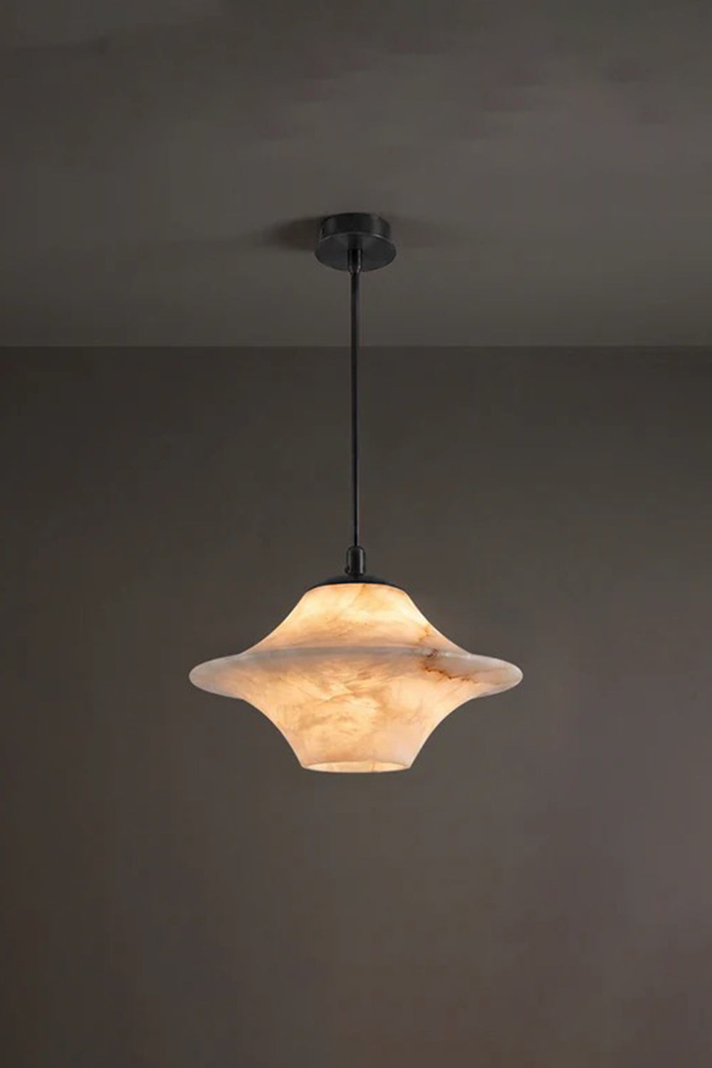 Thalia Alabaster Flared Pendant Light | Alabaster, Metal | Studio view of the illuminated alabaster flared ceiling fixture casting a rich amber halo against a dark moody charcoal backdrop | Samu Lamp