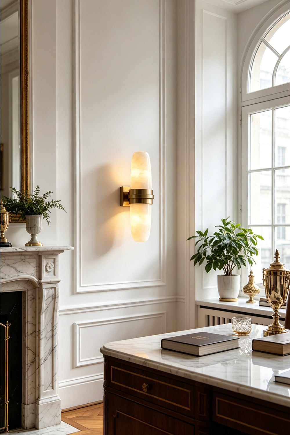 Theron Linear Alabaster Wall Lamp | Alabaster, Metal | Wall sconce casting a warm ambient glow near a classical white fireplace mantel and large bright windows | Samu Lamp