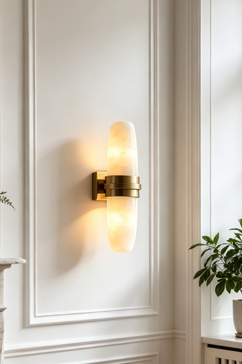 Theron Linear Alabaster Wall Lamp | Alabaster, Metal | Close-up shot of the fully lit capsule lamp casting a warm bi-directional glow on a white decorative wall panel | Samu Lamp
