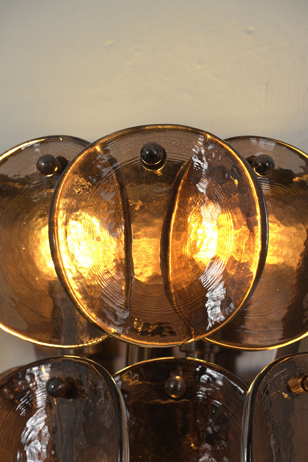 Tisanne Tiered Glass Disc Wall Lamp | Smoked Glass and Metal | Close-up view of glowing smoked amber glass discs illuminated warmly | Samu Lamp