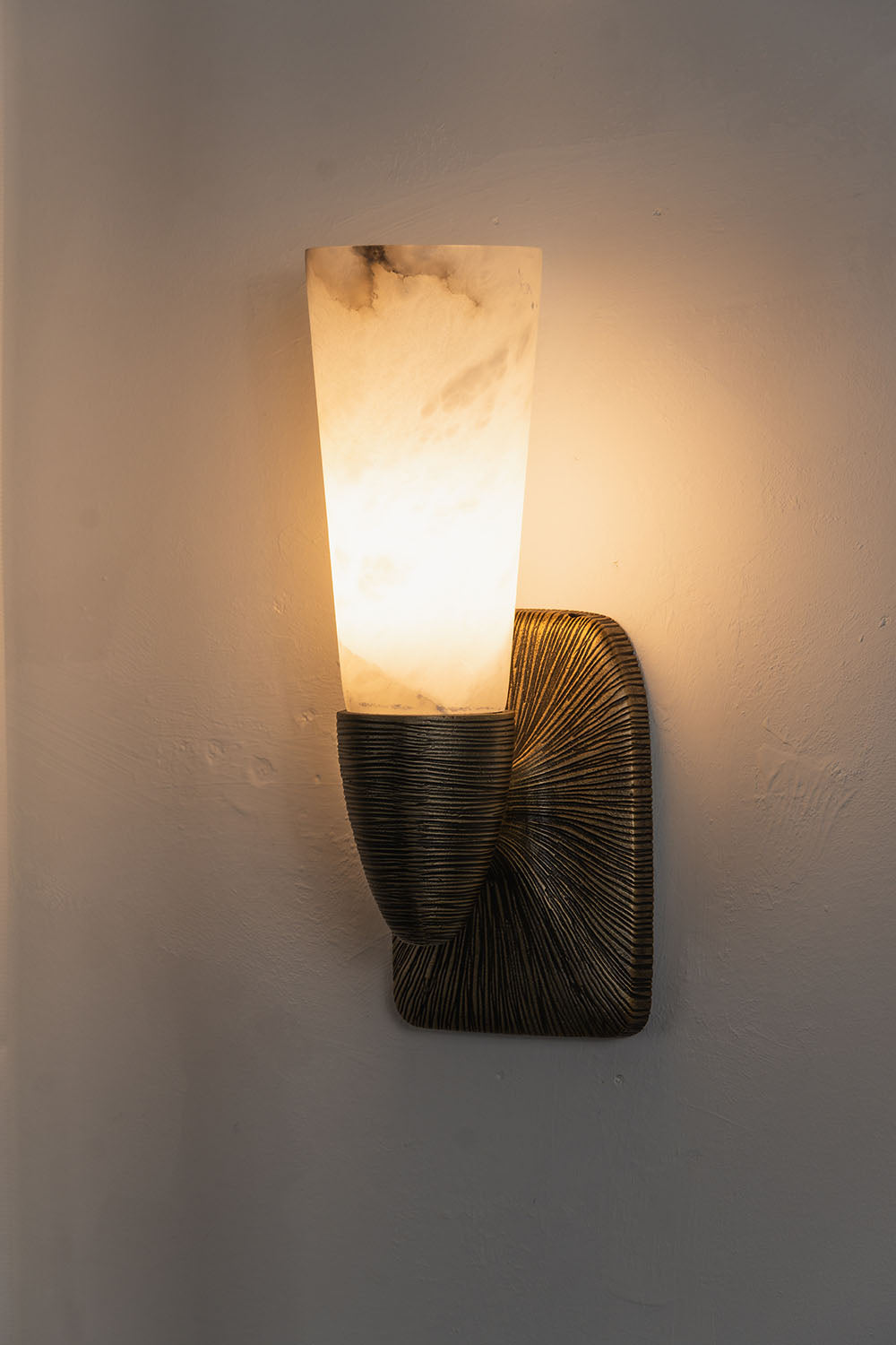 Torsanne Wall Sconce | Alabaster and Bronze | Single-light model lit at an angle against grey wall | Samu Lamp