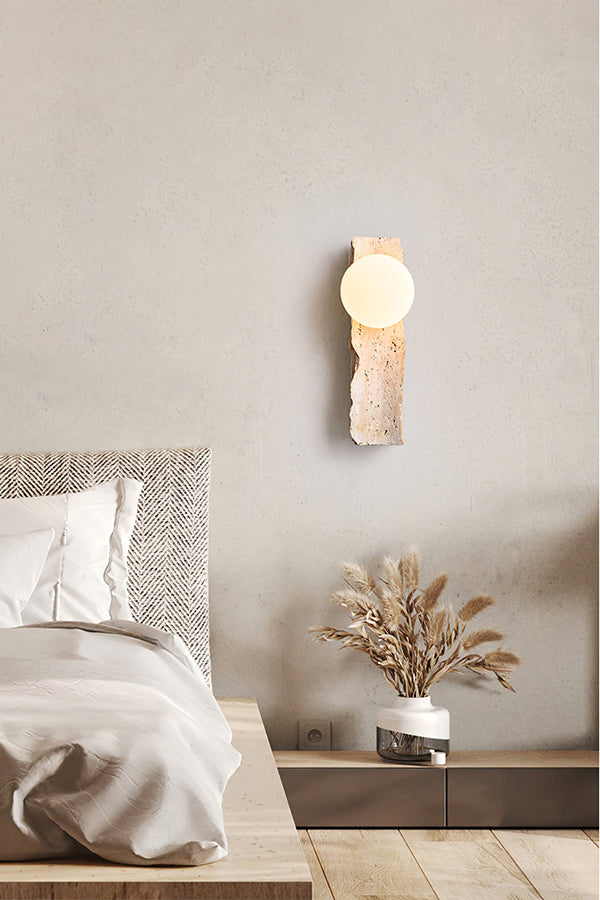 Travertine block wall sconce in a serene bedroom | Yellow Travertine, Metal, Glass | Mounted on a textured wall above the bed | Samu Lamp