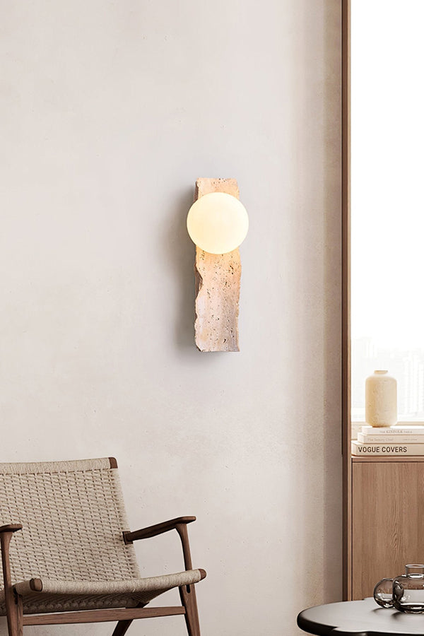 Minimalist stone wall lamp in bright interior | Yellow Travertine, Metal, Glass | Mounted on a clean wall near a wooden chair | Samu Lamp