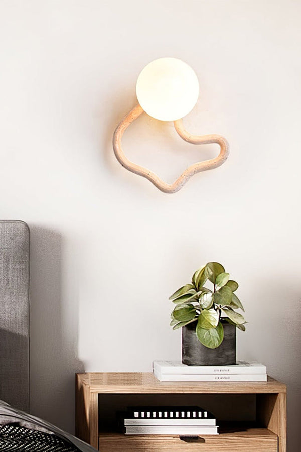 Modern travertine wall light with organic shape | Travertine, Glass, Wood | Mounted above a wooden nightstand with a small plant | Samu Lamp
