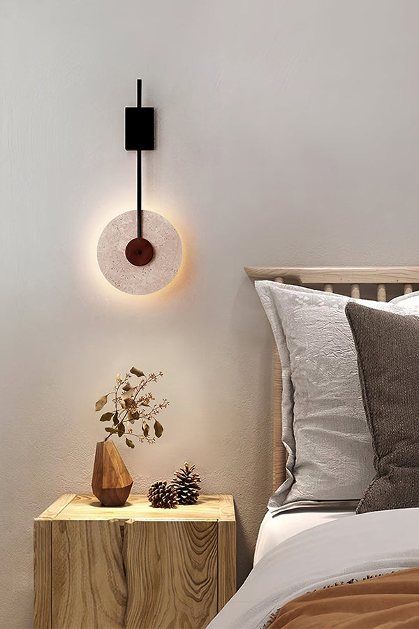 Lit travertine halo sconce over a wooden bedside table | Travertine, Wood, Metal | Cozy bedroom scene with soft textures | Samu Lamp